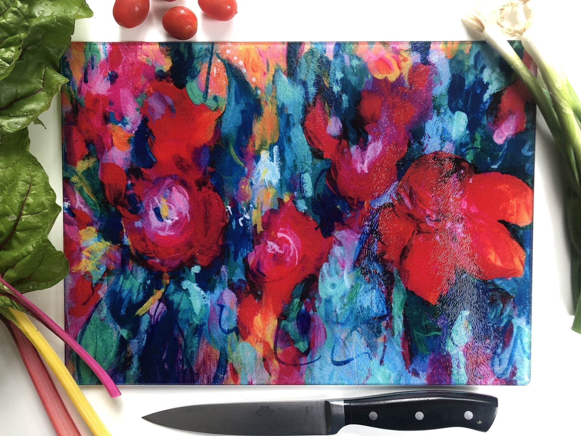 Colorful floral abstract design on a cutting board with a knife and vegetables.