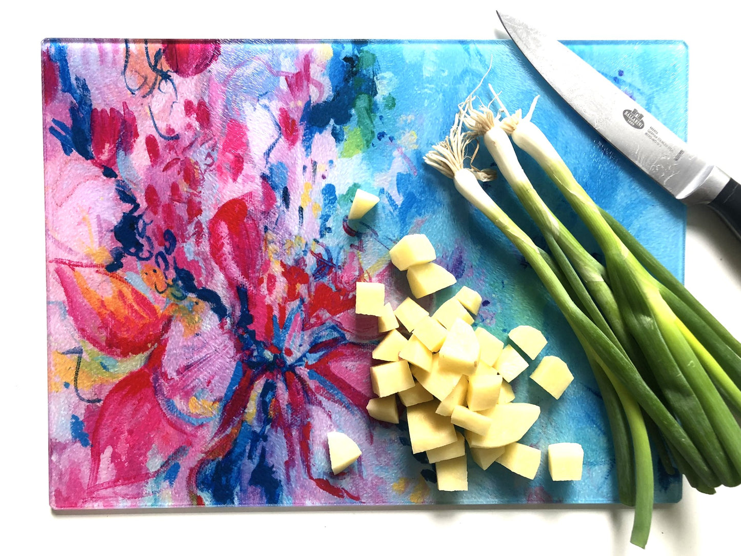 Colorful floral-patterned cutting board with chopped vegetables and a knife on a white background