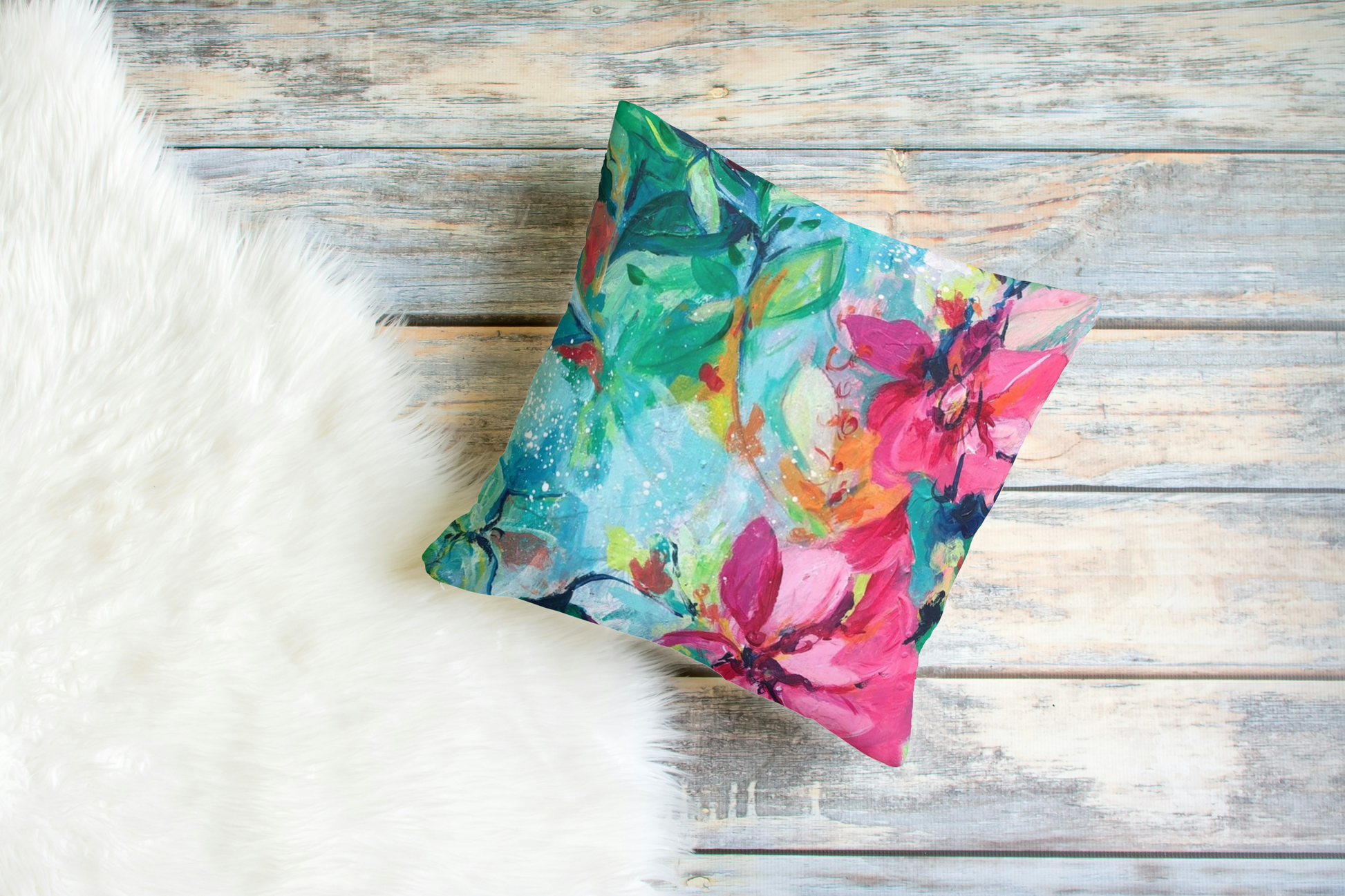 Pretty pink , green and aqua coloured floral cushion shown against wooden floorboards and a white , fluffy rug.