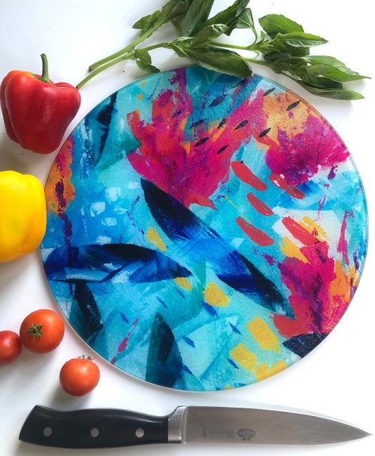 Colourful pink, blue and turquoise Tropical Seas glass chopping board shown with bright vegetables and a knife