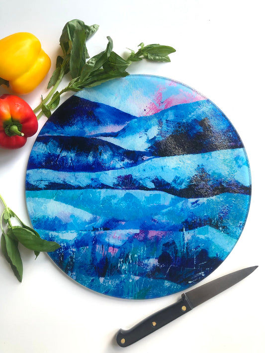 Tranquility blue and pink arty glass cutting board shown with a knife and colourful vegetables