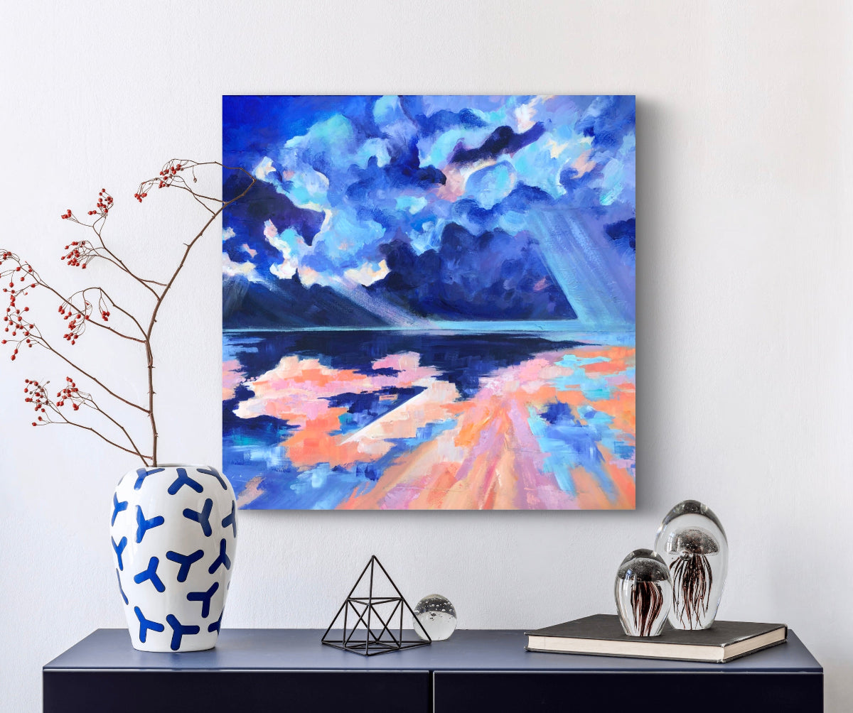 Colourful square painting of beach and sky displayed above a navy blue  cabinet