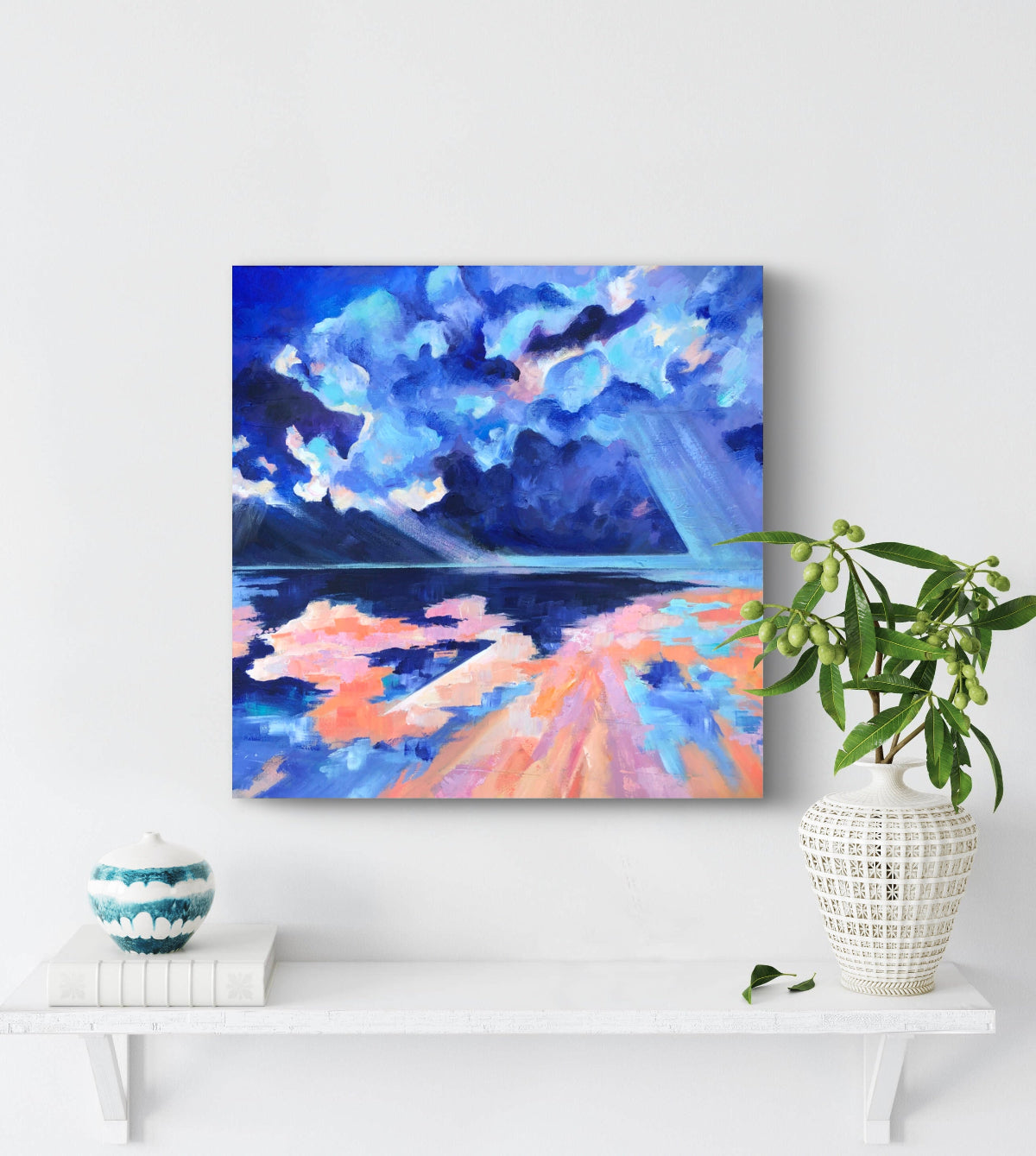 Colourful, bright and modern painting of beach and sky displayed against a white wall and next to a vase of lush foliage