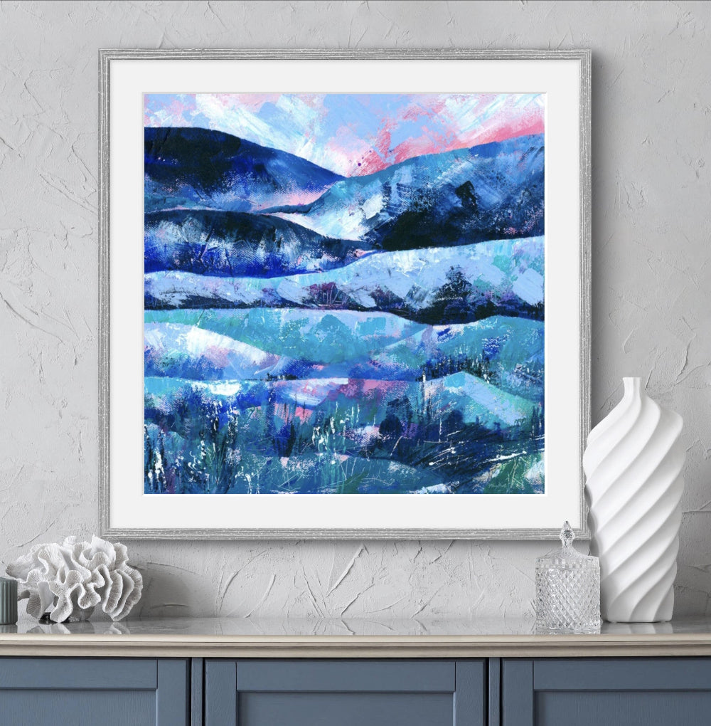 Abstract landscape art print with rolling hills and pink sunset shown framed with blue furniture