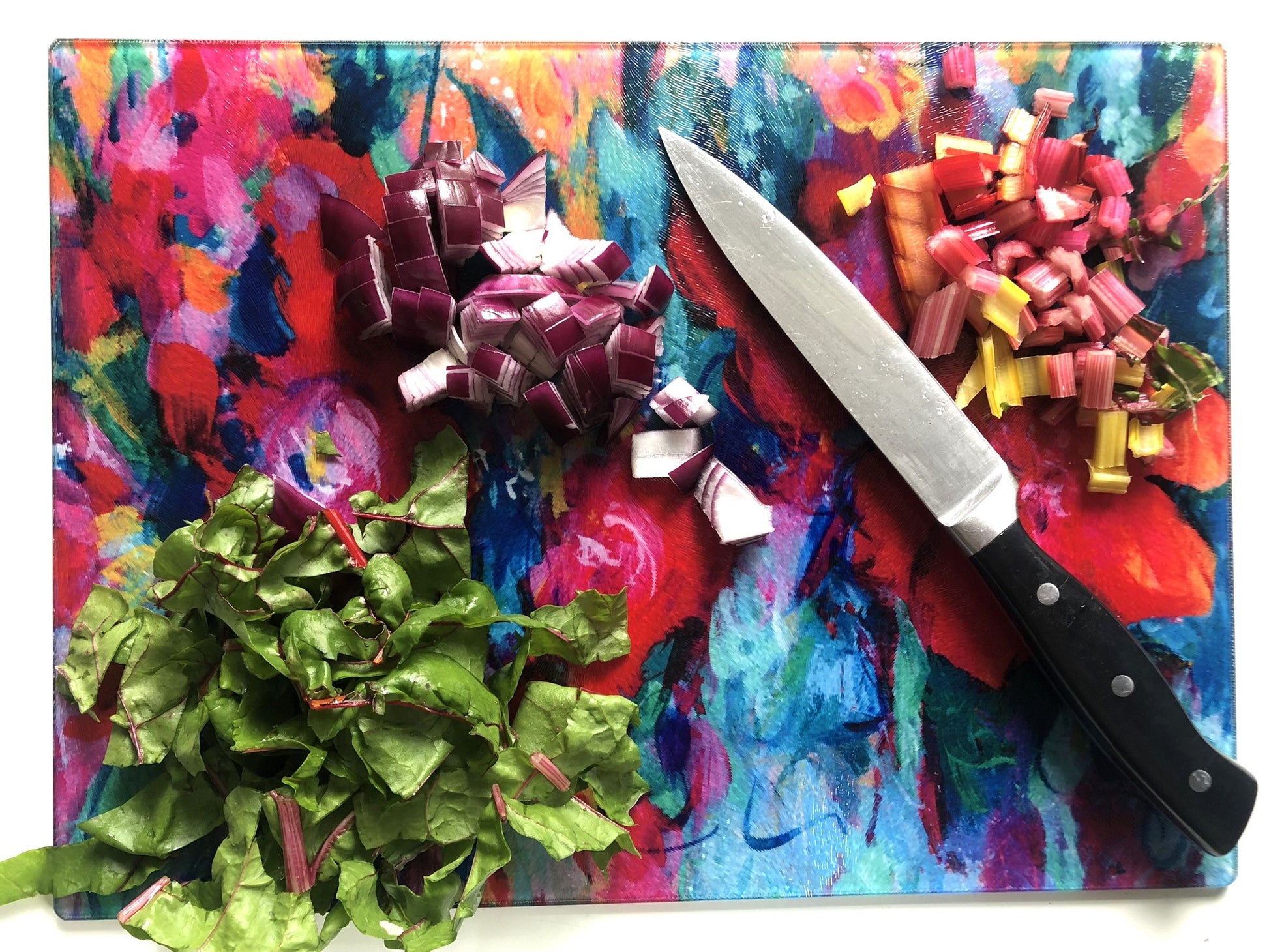 Colorful cutting board with a knife, vegetables, and a decorative flower on a white background