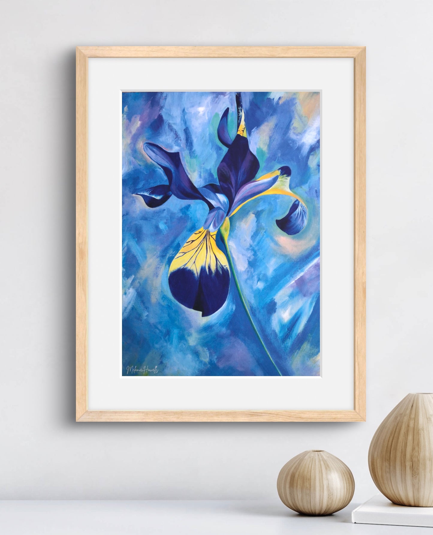 Framed wall art featuring an expressive blue and purple iris painting with yellow accents, displayed in a light wood frame on a white wall above a surface with two decorative vases.