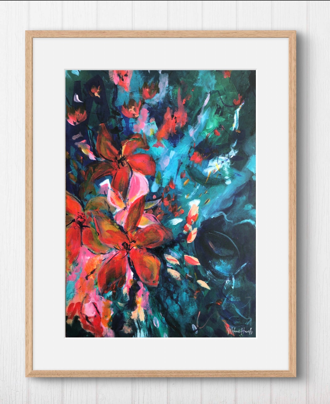 Framed abstract floral wall art print with expressive brushstrokes in red, orange, teal, and dark blue, set in a light wood frame against a white paneled wall.