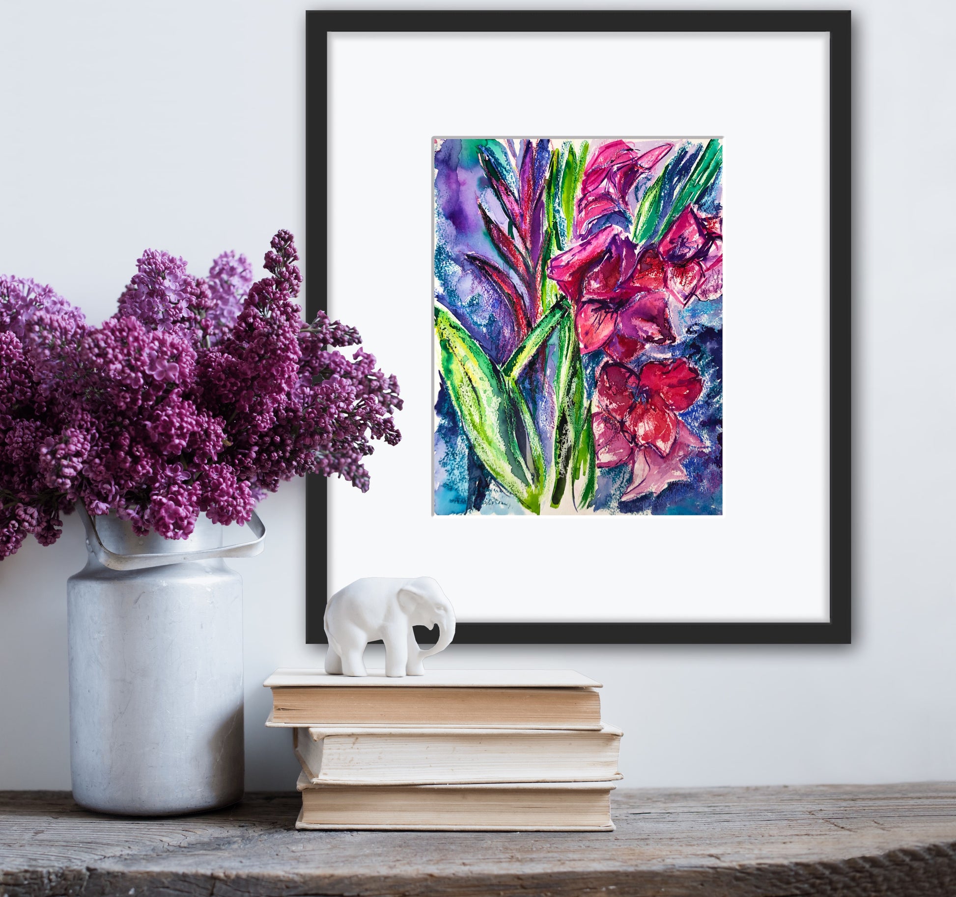 Gladioli original floral painting displayed with a white mount and a simple black frame against a white wall with books and a vase of lilacs nearby.