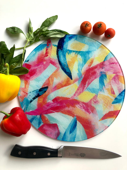 Adventure multicoloured abstract art glass chopping board shown with vegetables and a knife around it.