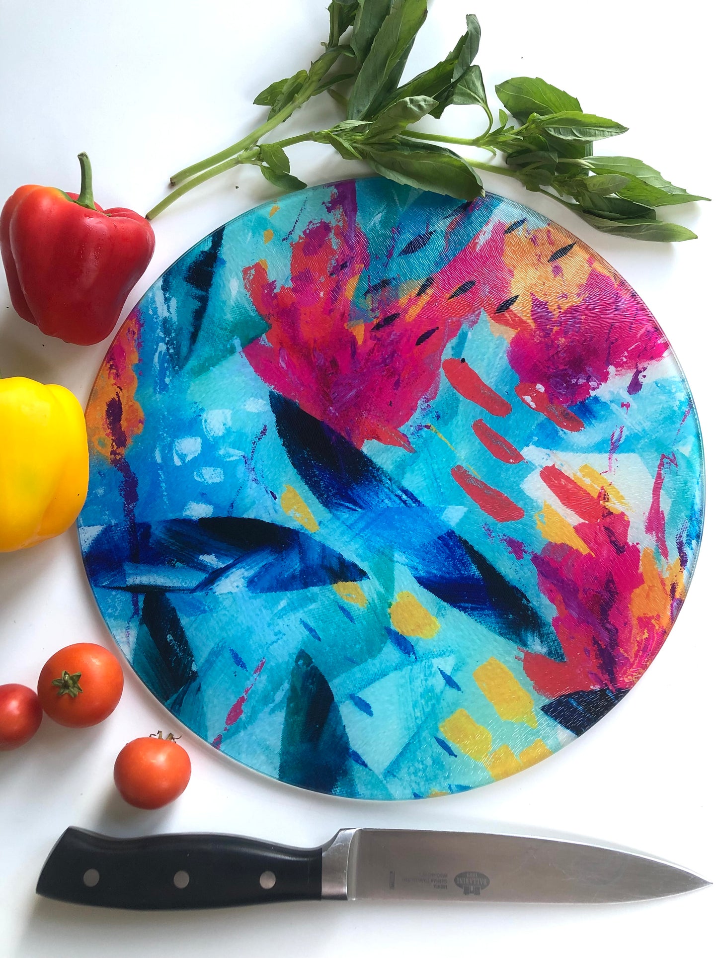 Colourful pink, blue and turquoise Tropical Seas glass chopping board shown with bright vegetables and a knife