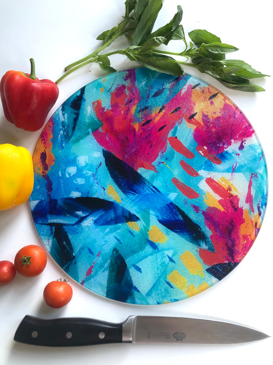 Colourful pink, blue and turquoise Tropical Seas glass chopping board shown with bright vegetables and a knife