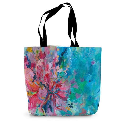 A colourful canvast tote bag featuring a bright floral design in pinks, turquoise and green. Features black handles.