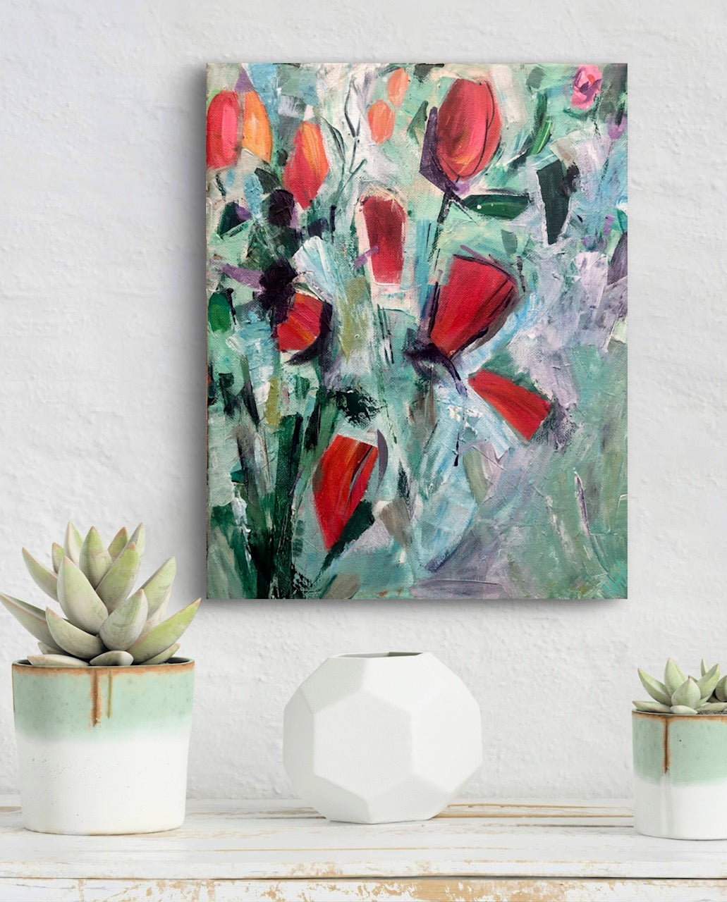 Abstract painting with red flowers on a white wall above a shelf with decorative items.