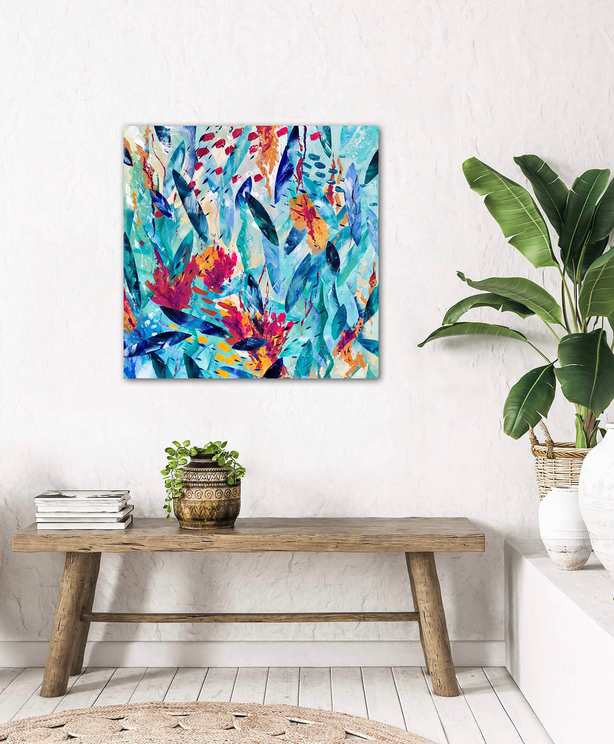 Colourful abstract acrylic painting on stretched canvas called Tropical Dreams. Measures 60x60cm and features shades of pink, blue, turquoise and orange. Displayed on a white wall near a rustic wooden bench and large pot plant..