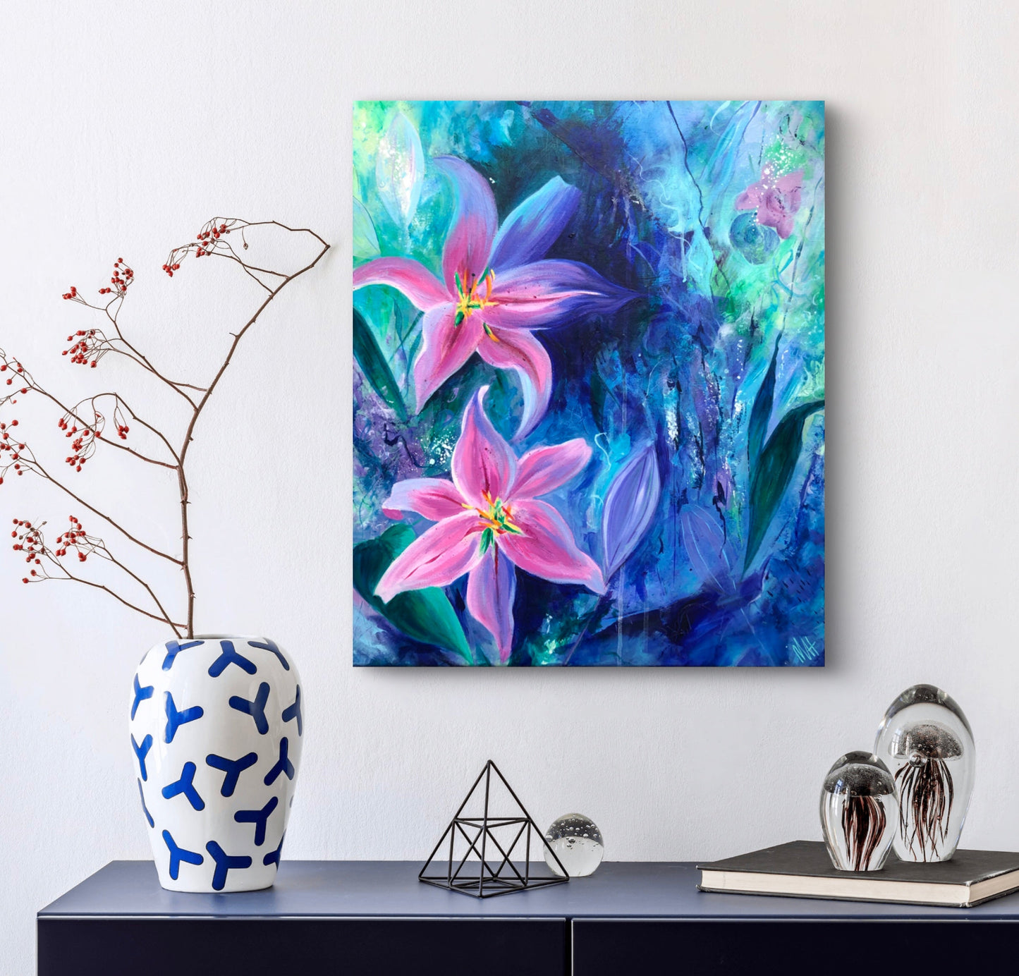 An original painting of pink lilies against a textured and rich blue background, displayed on a neutral wall above a piece of dark blue side board with a vase.